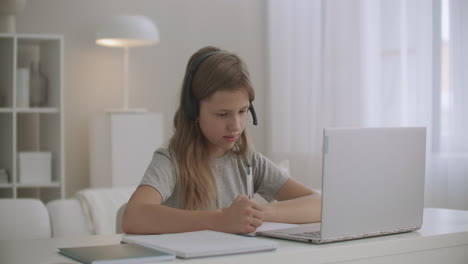 homeschooling-for-children-online-girl-is-communicating-with-teacher-by-headphones-and-video-chat-on-laptop-writing-in-copybook